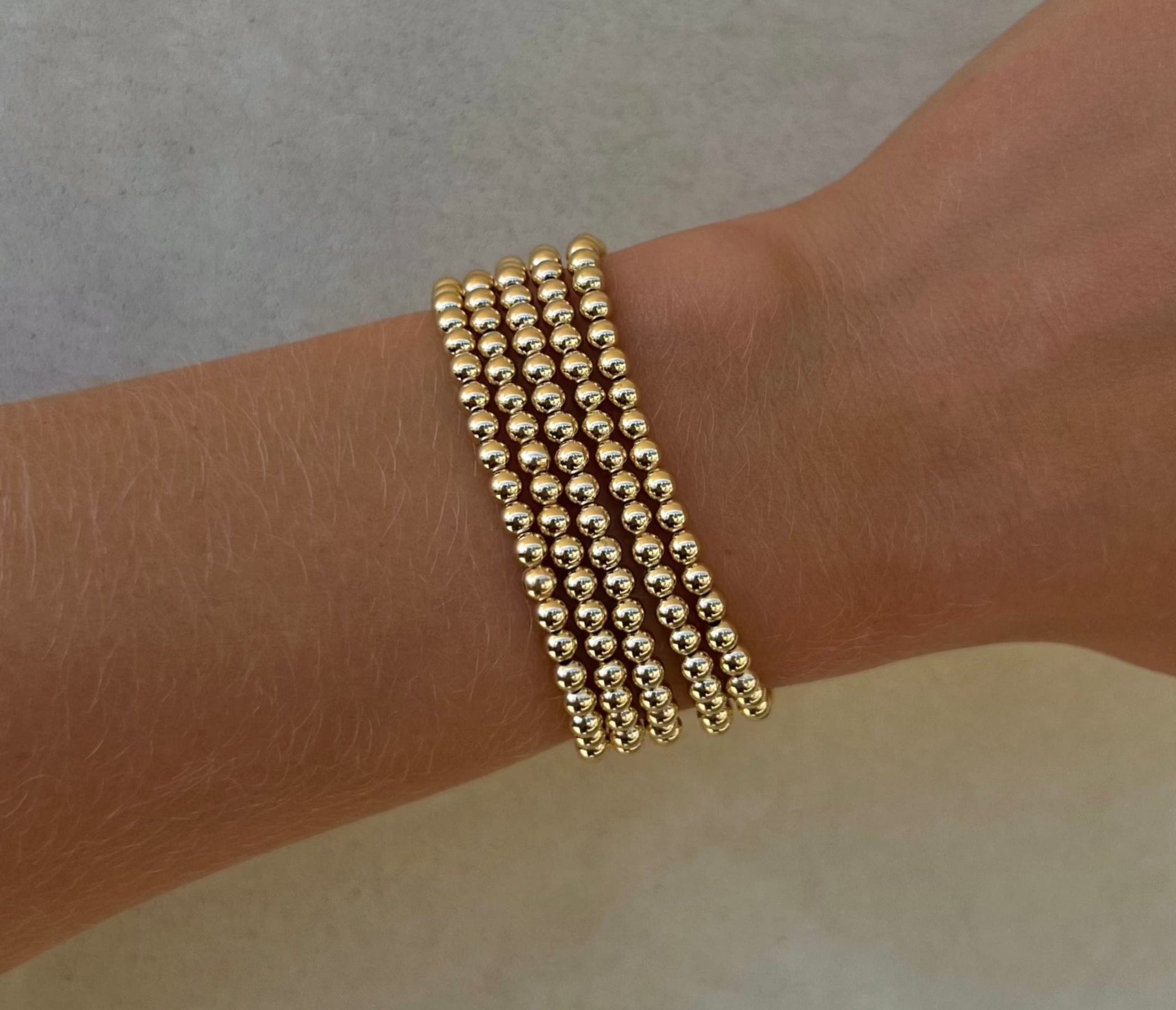 Five gold beaded bracelets with 4mm spheres worn on wrist.