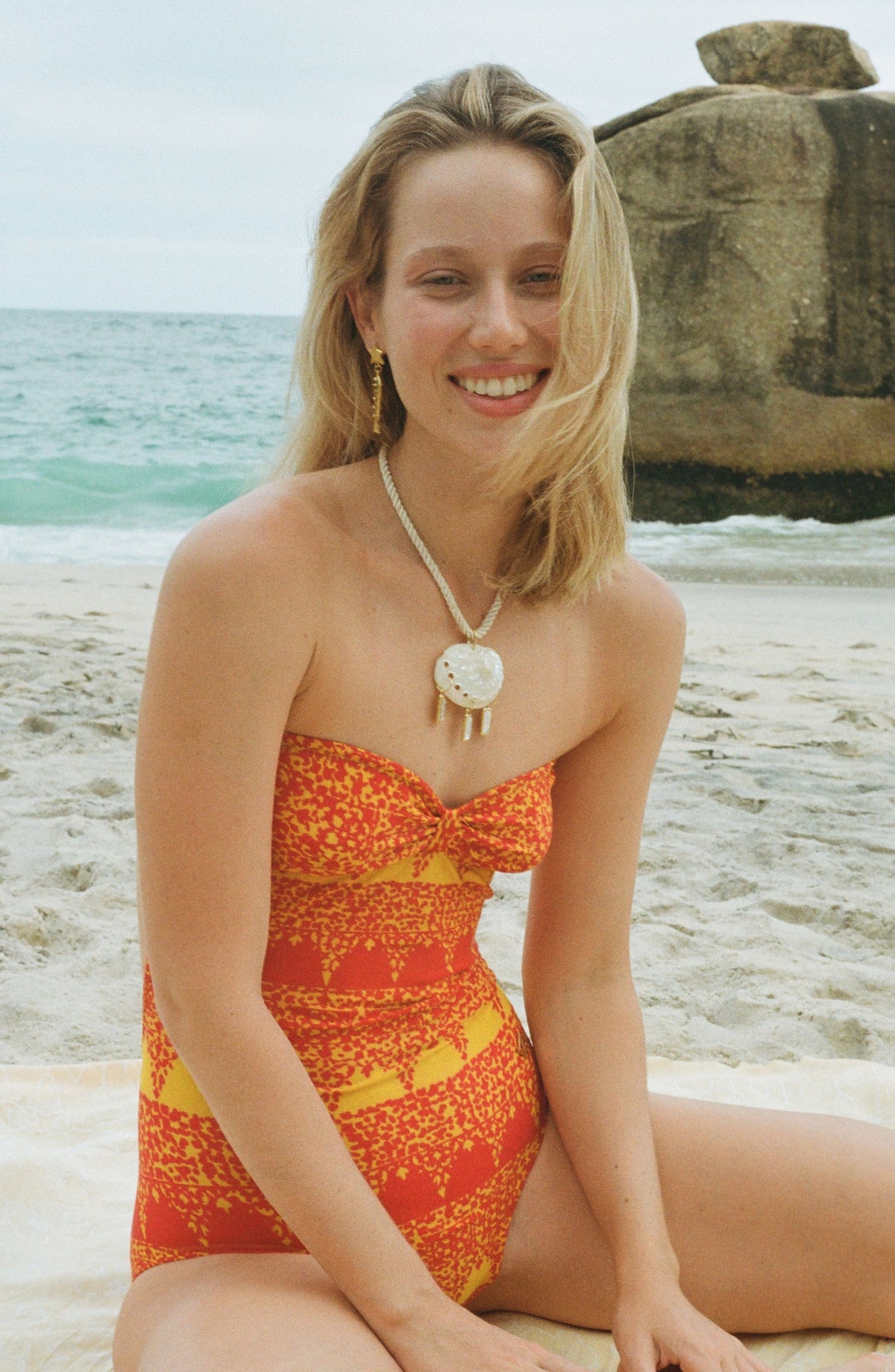 White beaded choker necklace with circular shell pendant and tassel detail worn at the neck.