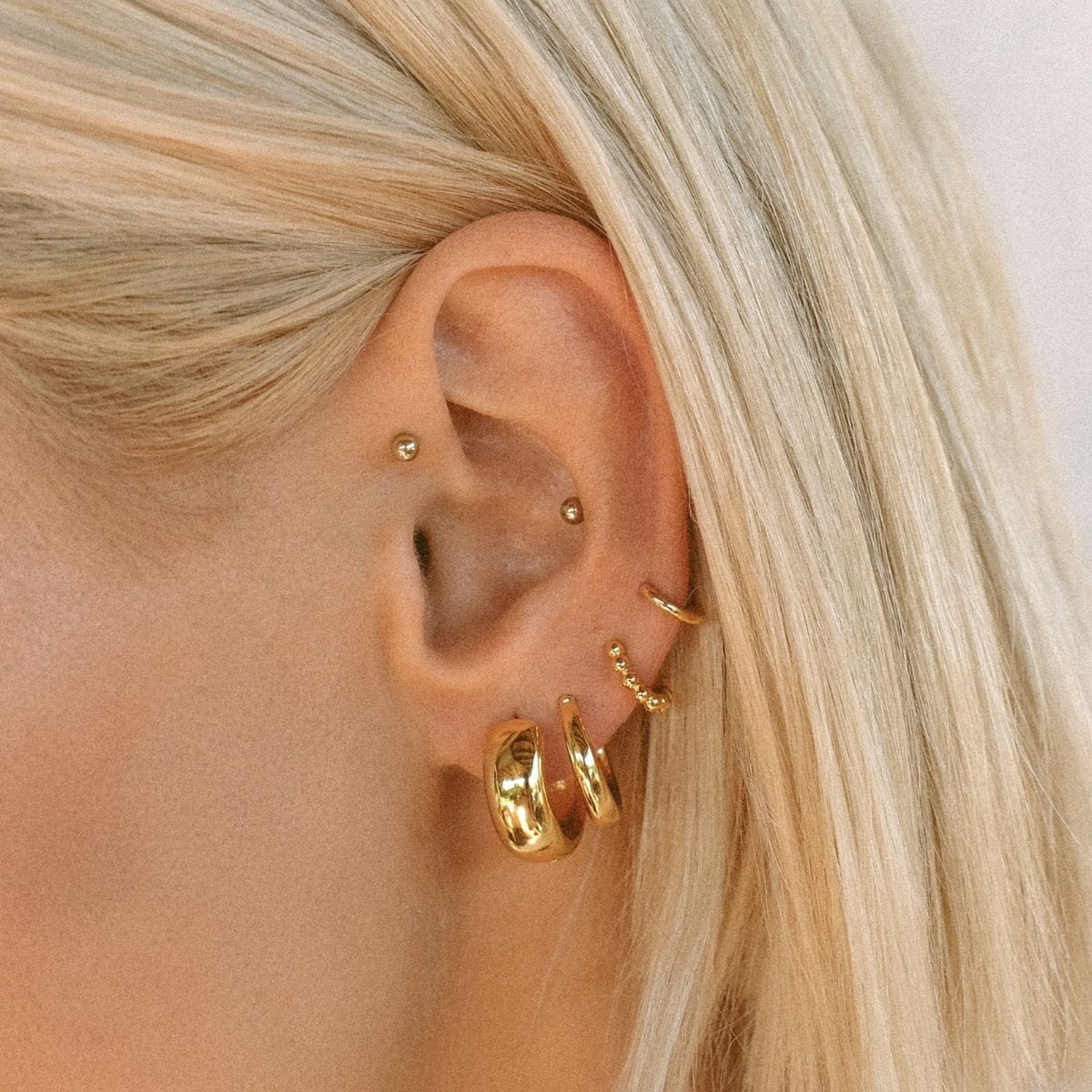 Gold chunky hoop earrings worn on earlobe with additional piercings visible on upper ear.