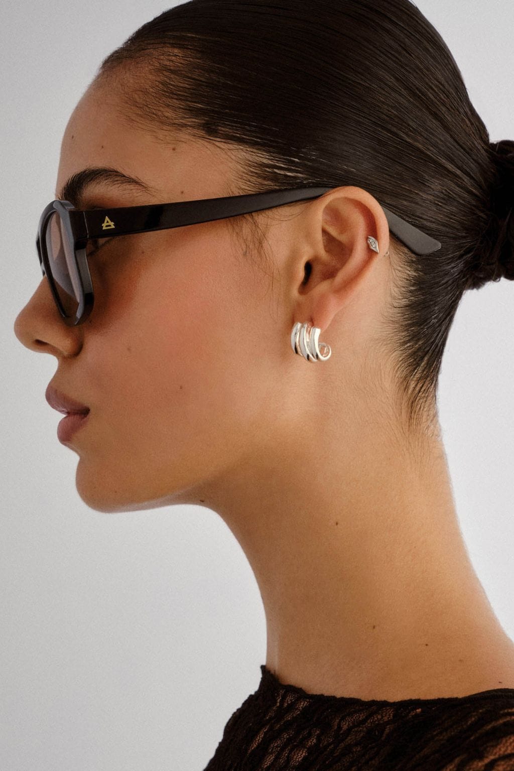 Black oval sunglasses with dark lenses and gold-toned temple accents worn by a person in profile.