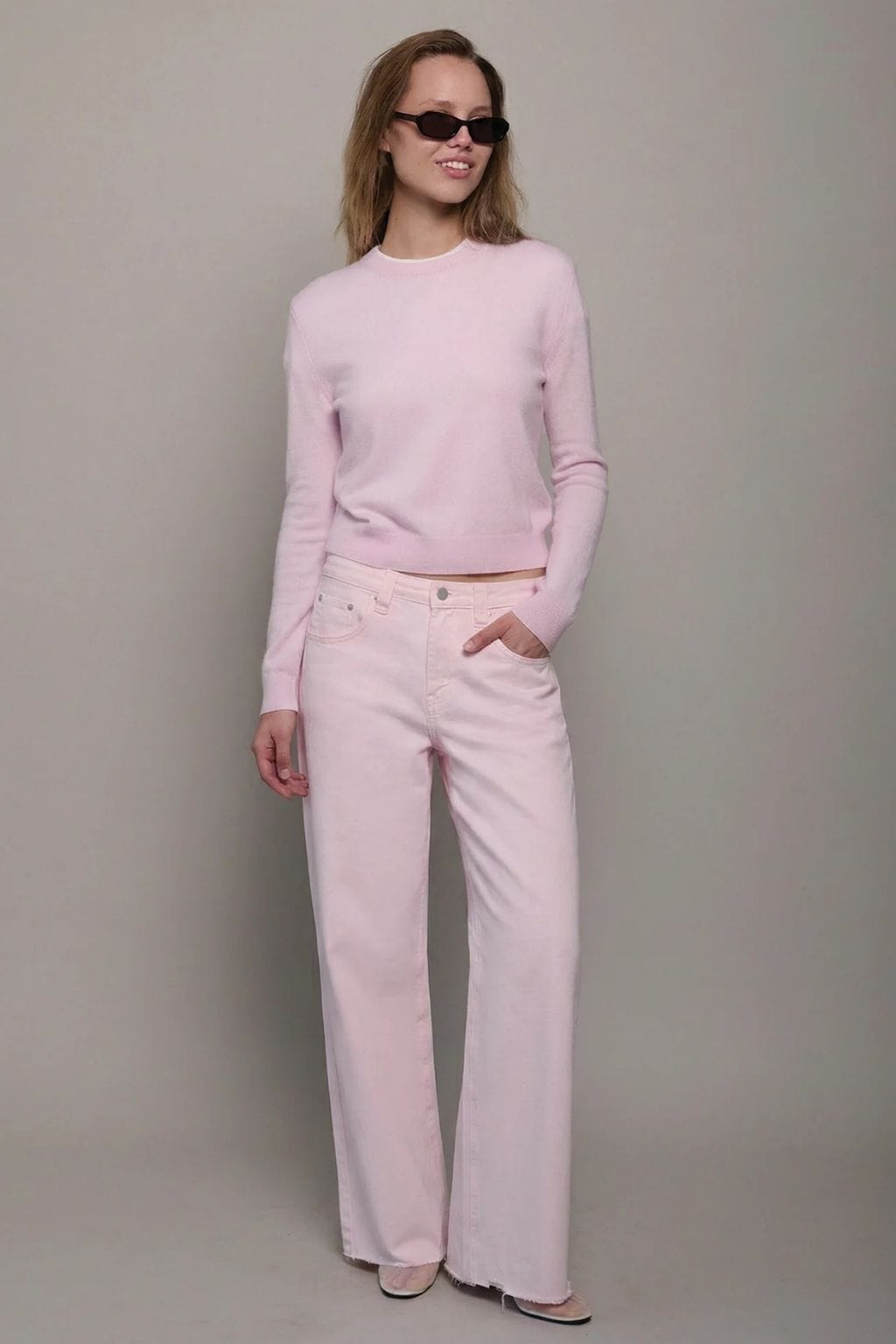 Woman wearing light pink long-sleeve crew neck sweater and matching wide-leg jeans with sunglasses.