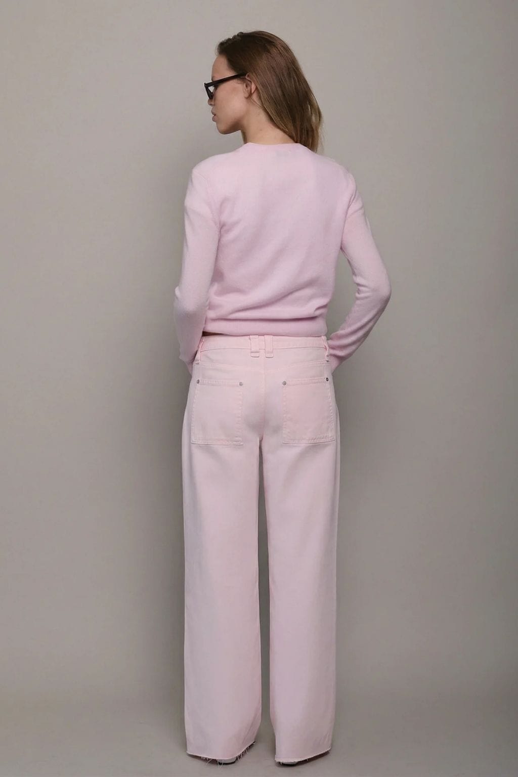 Woman wearing light pink long-sleeve sweatshirt and matching wide-leg jeans with back pockets, shown from behind.