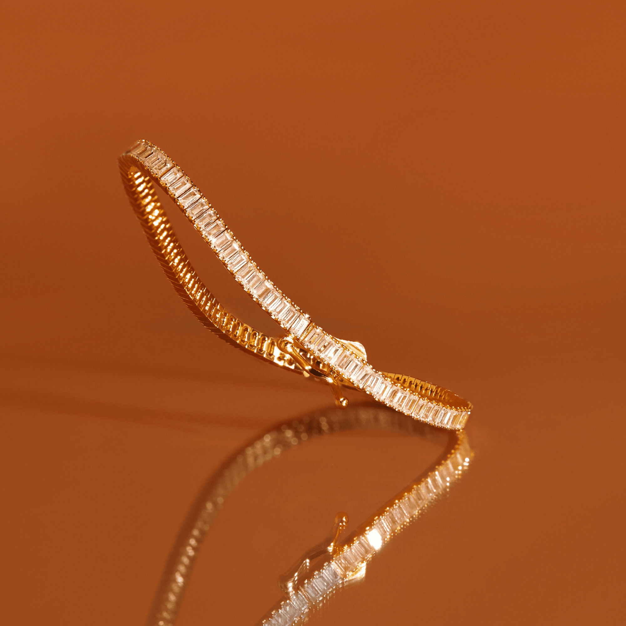 Gold tennis bracelet with rectangular clear stones set in a continuous line around the band.