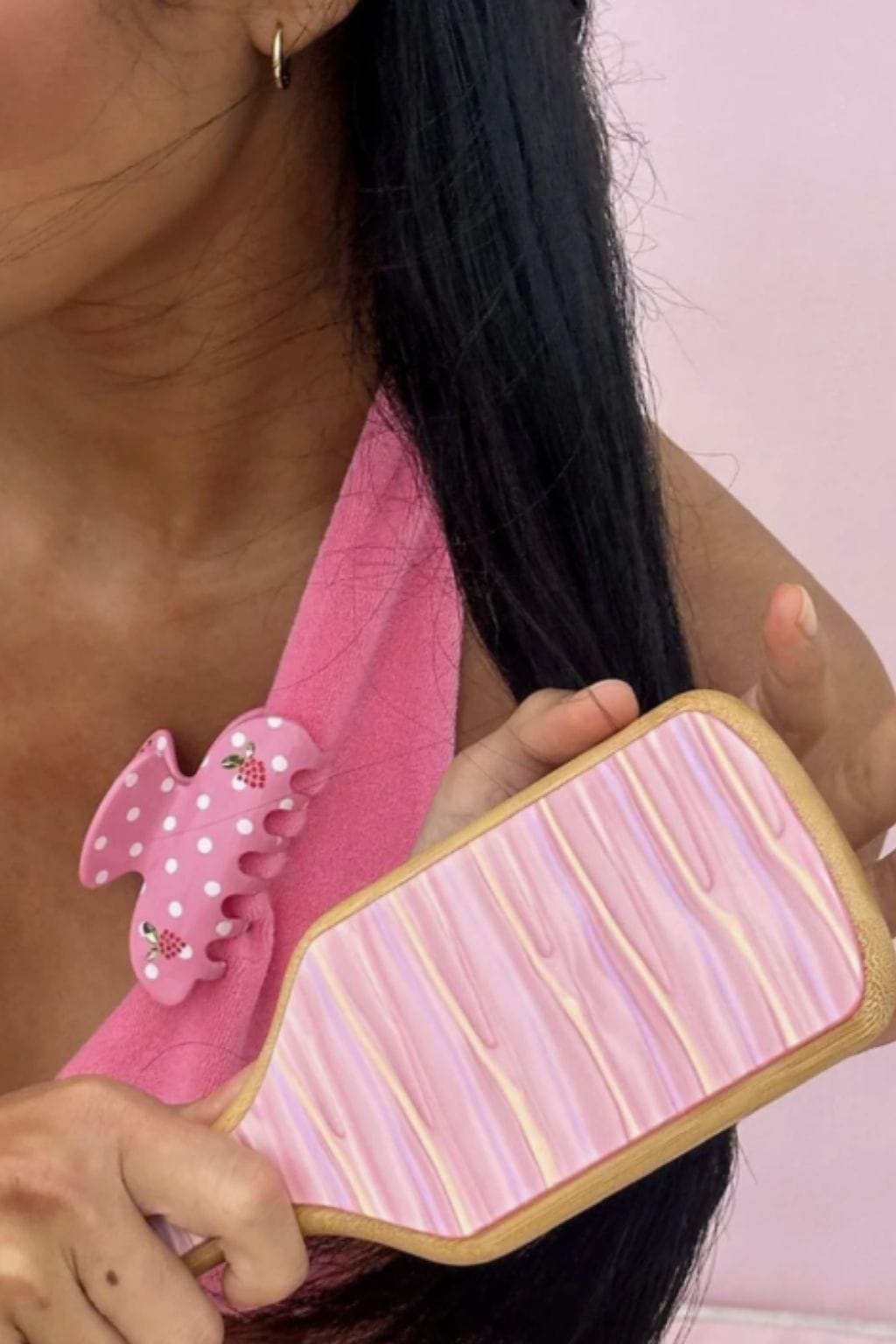 Pink paddle brush with white polka dots and lychee details, held against black hair.