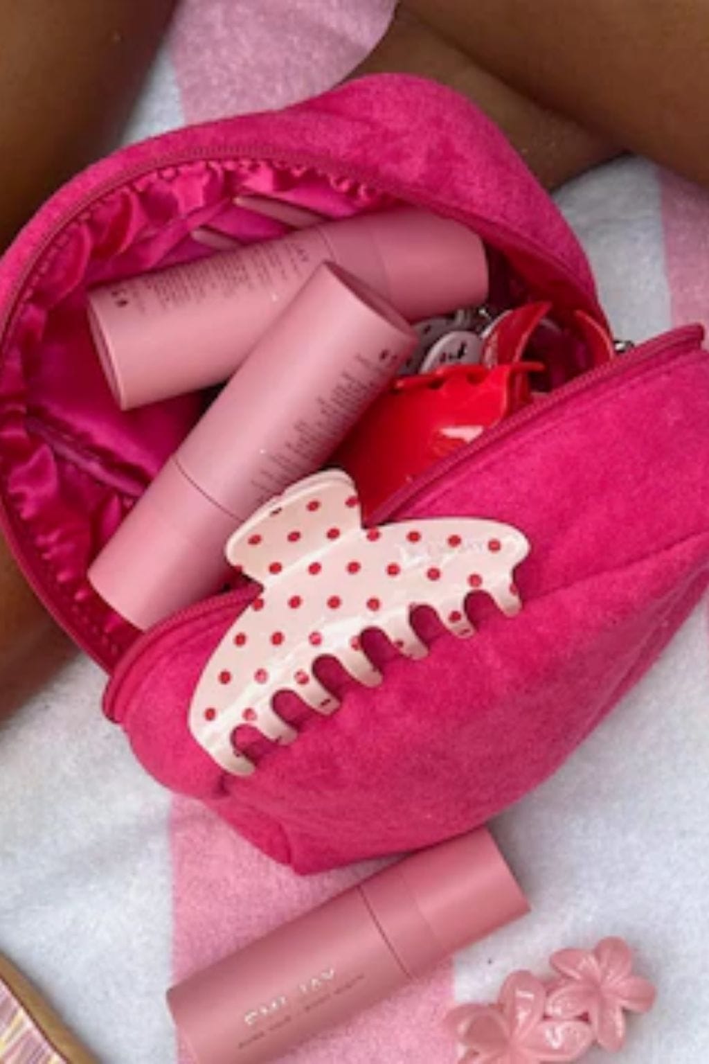Large pink hair clip with cream-colored claw design and red polka dots, displayed with beauty products inside pink pouch.