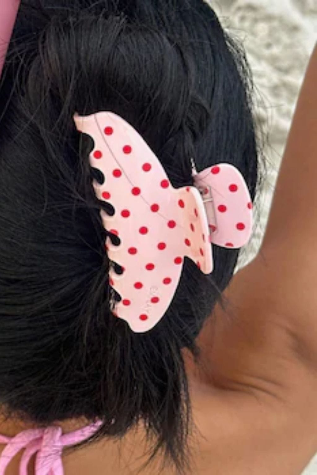 Blush pink bow-shaped hair clip with red polka dots, clipped into black hair.