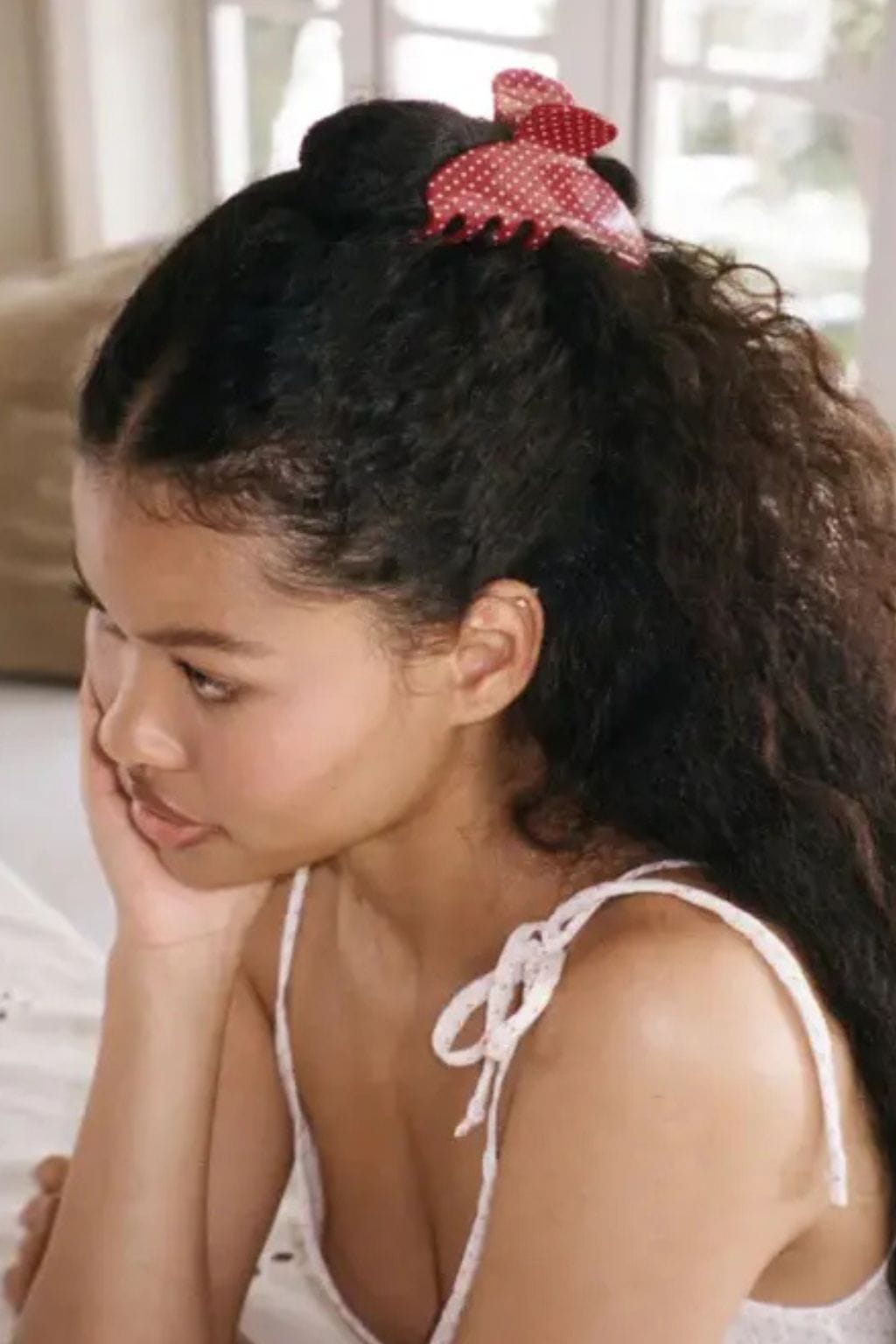Red polka dot hair clip holding back dark hair on a person shown in profile.