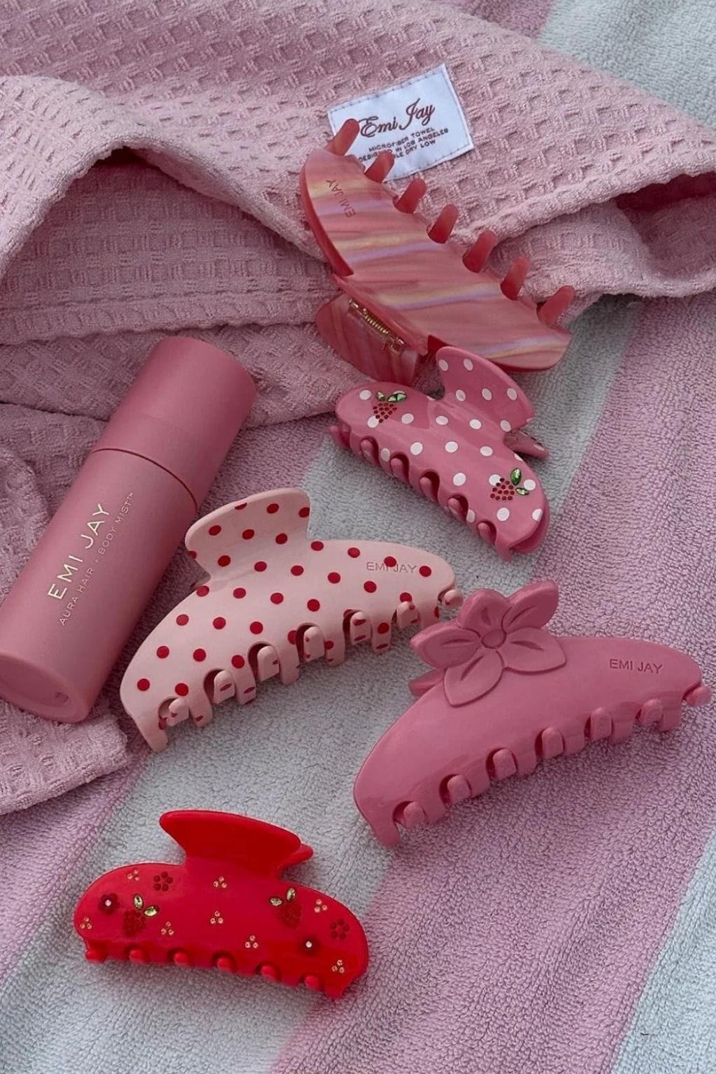 Large pink hair clip with curved claw design and decorative details, displayed with matching smaller clips and a spray bottle