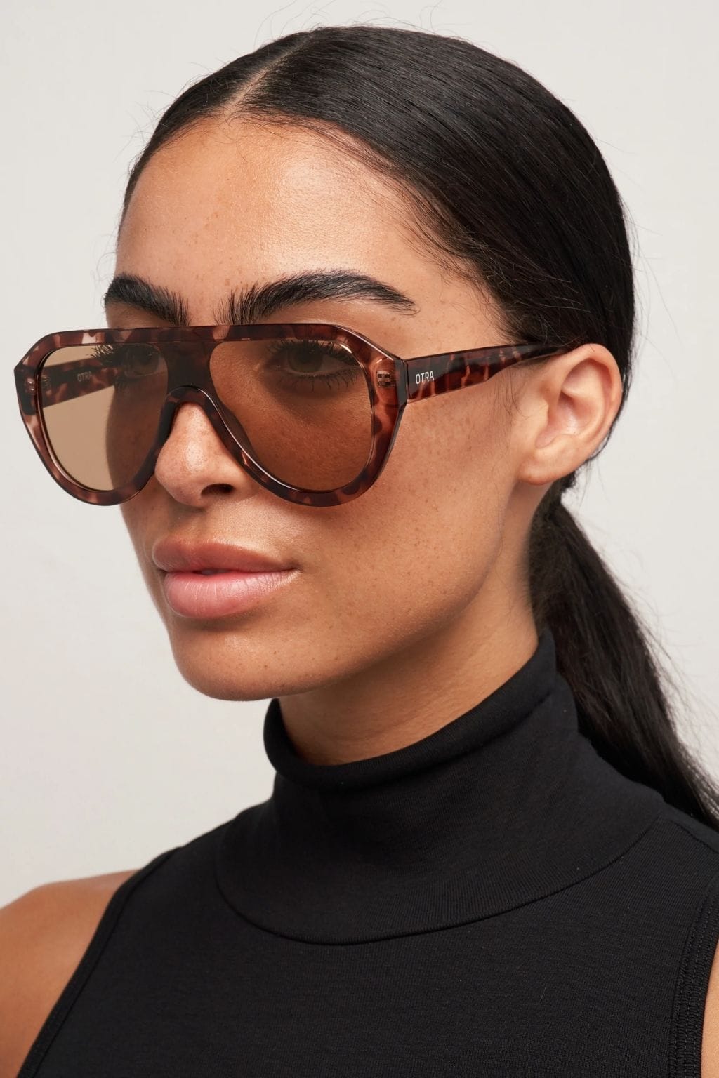 Tortoiseshell brown aviator sunglasses with brown tinted lenses worn by a person in a black turtleneck.