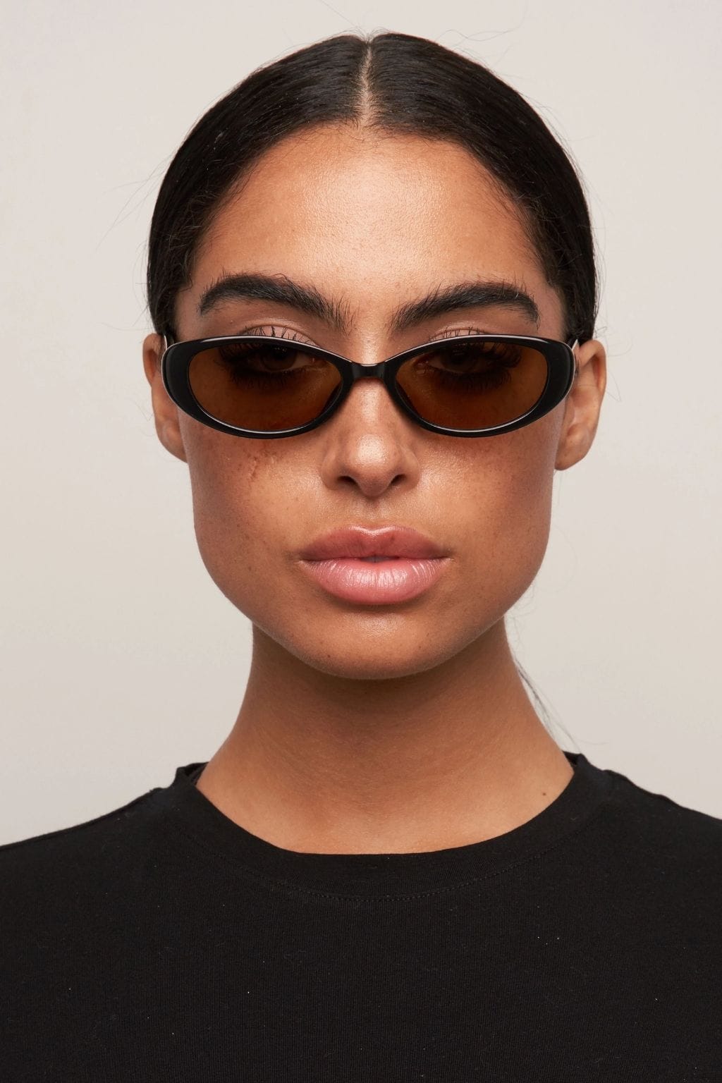 Black oval sunglasses with brown-tinted lenses worn by a person in a black top.