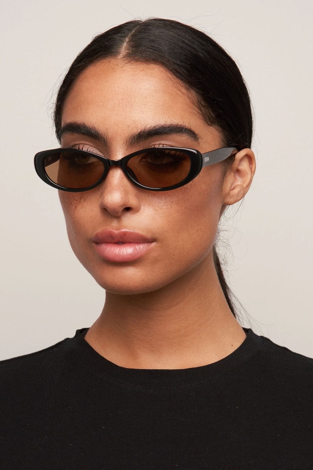 Black and brown oval sunglasses with dark tinted lenses on a person wearing a black top.