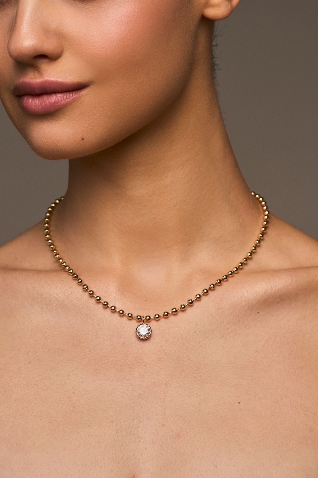 Gold ball chain necklace with round crystal pendant worn close to neck.