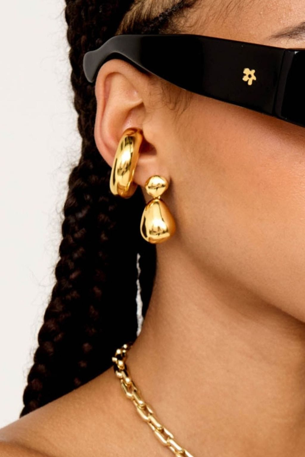 Pair of gold-toned drop earrings with polished teardrop pendants worn on model's ears.