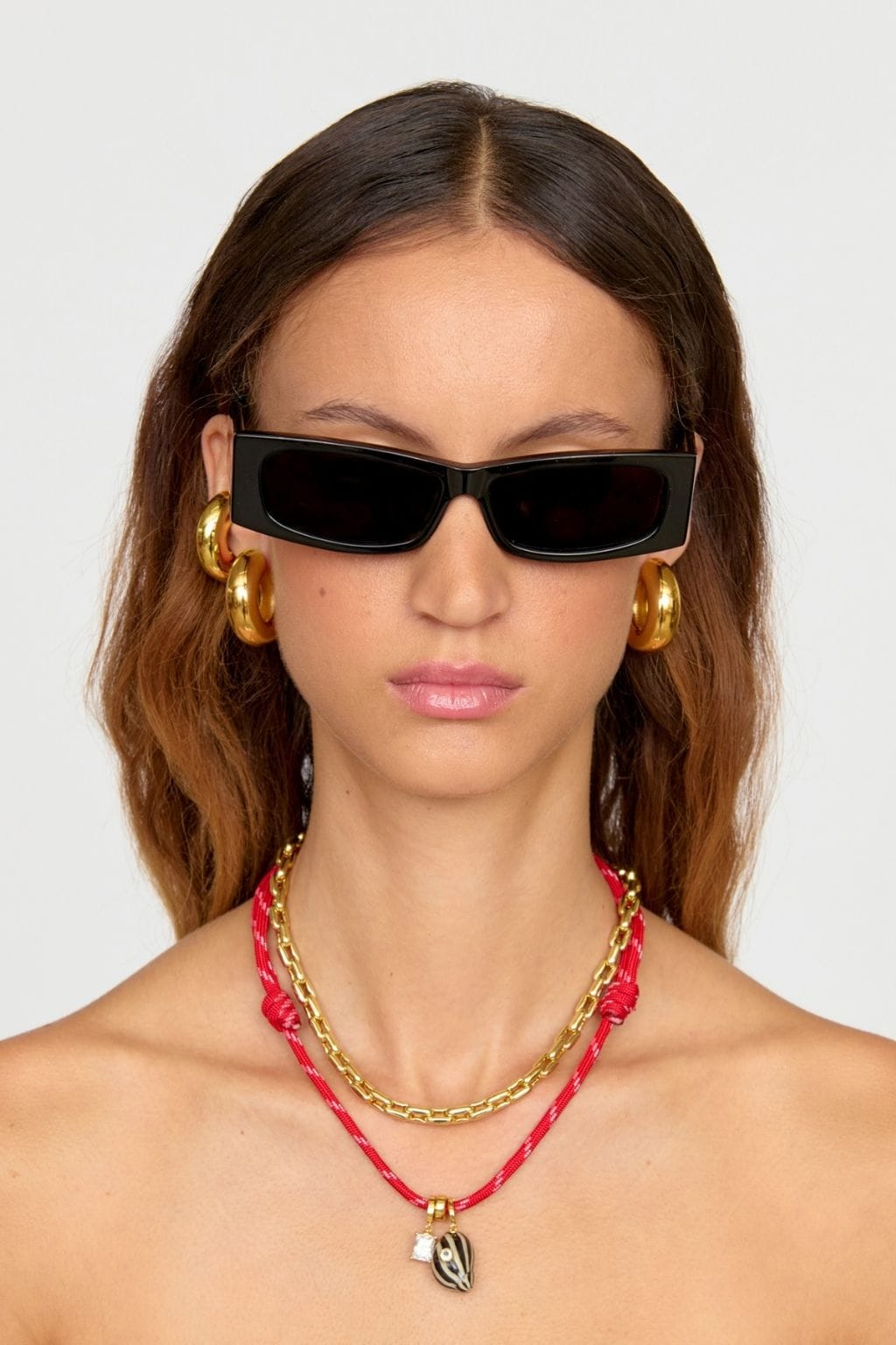 Gold chain necklace with pink cord and shell pendant worn layered with gold chain.