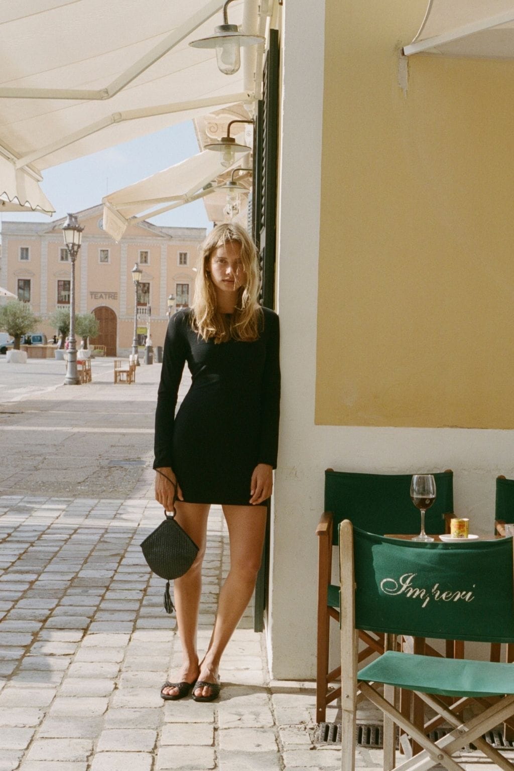 Black woven crossbody bag with rounded shape carried by woman in black dress.