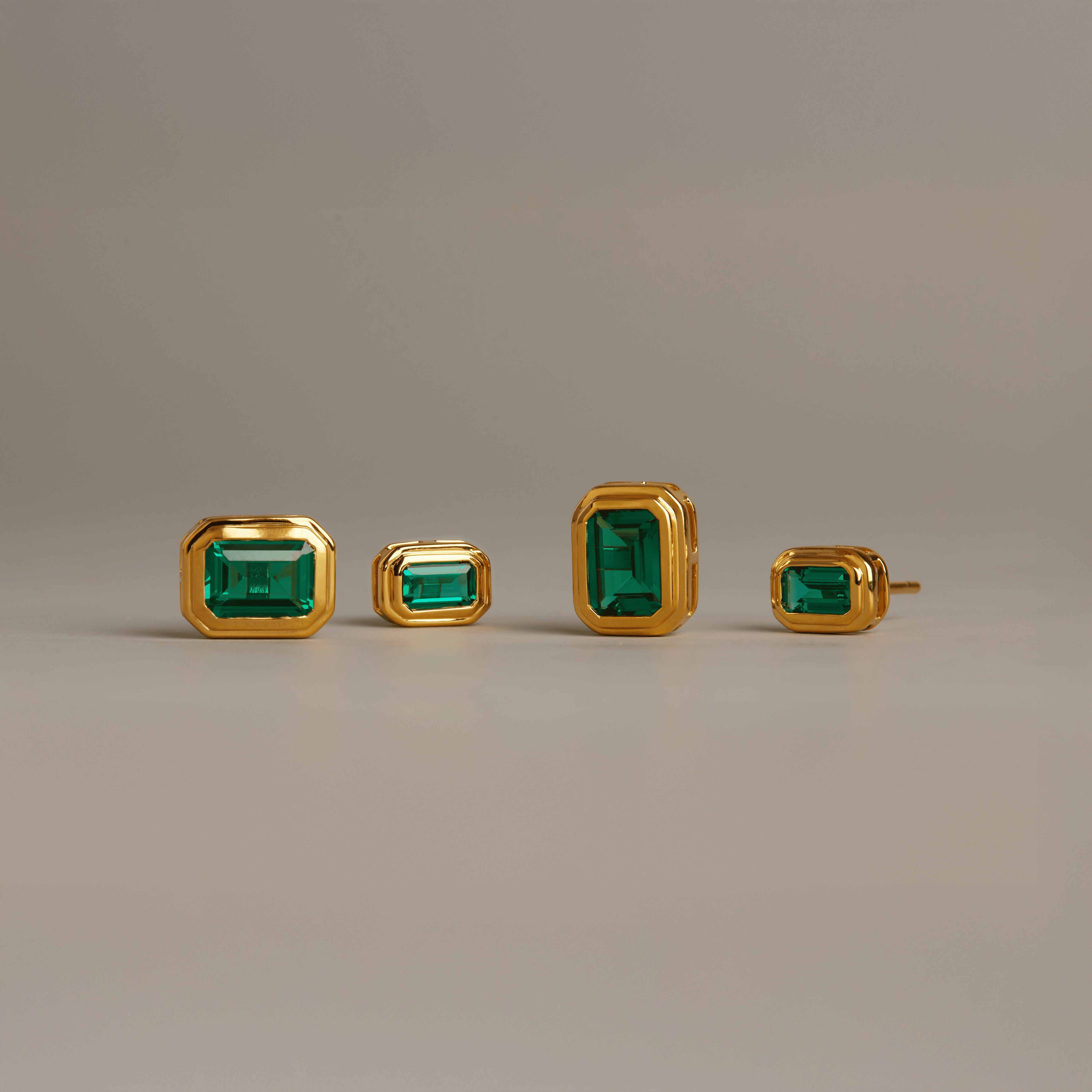 Four gold stud earrings with square-cut green emeralds in bezel settings, shown in varying sizes.