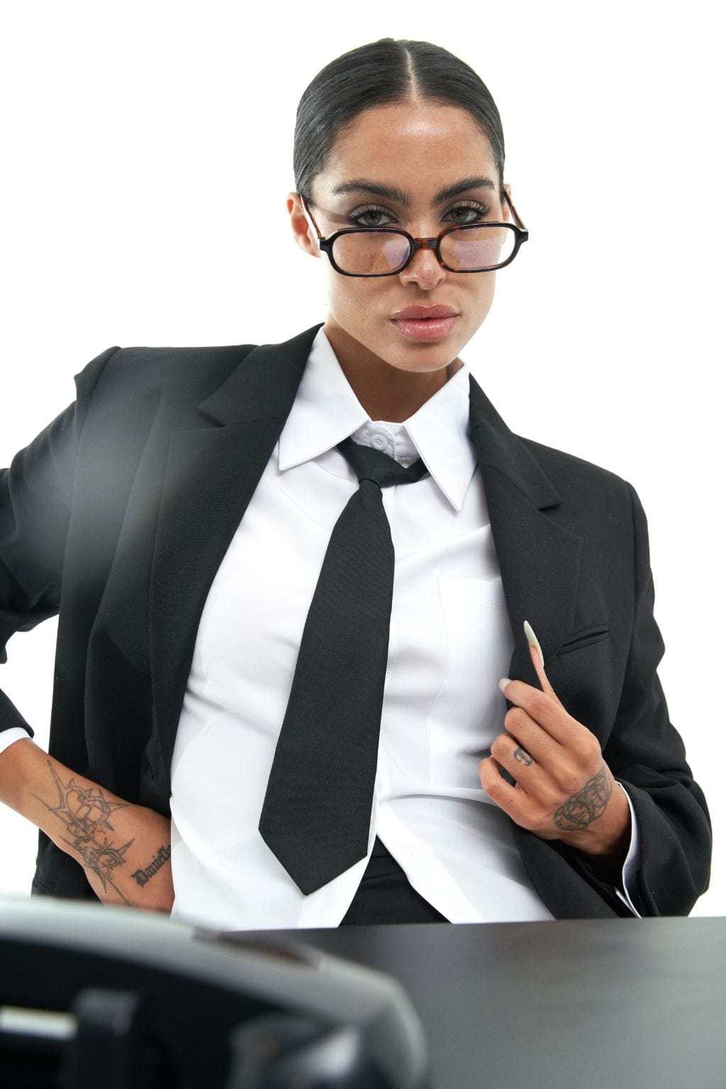 Woman wearing black rectangular eyeglasses with clear lenses, black blazer, and white dress shirt with black tie.