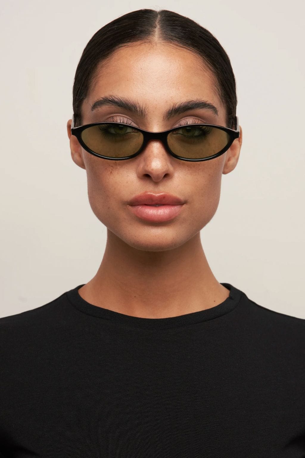 Black oval sunglasses with brown-tinted lenses worn by a person in a black shirt.