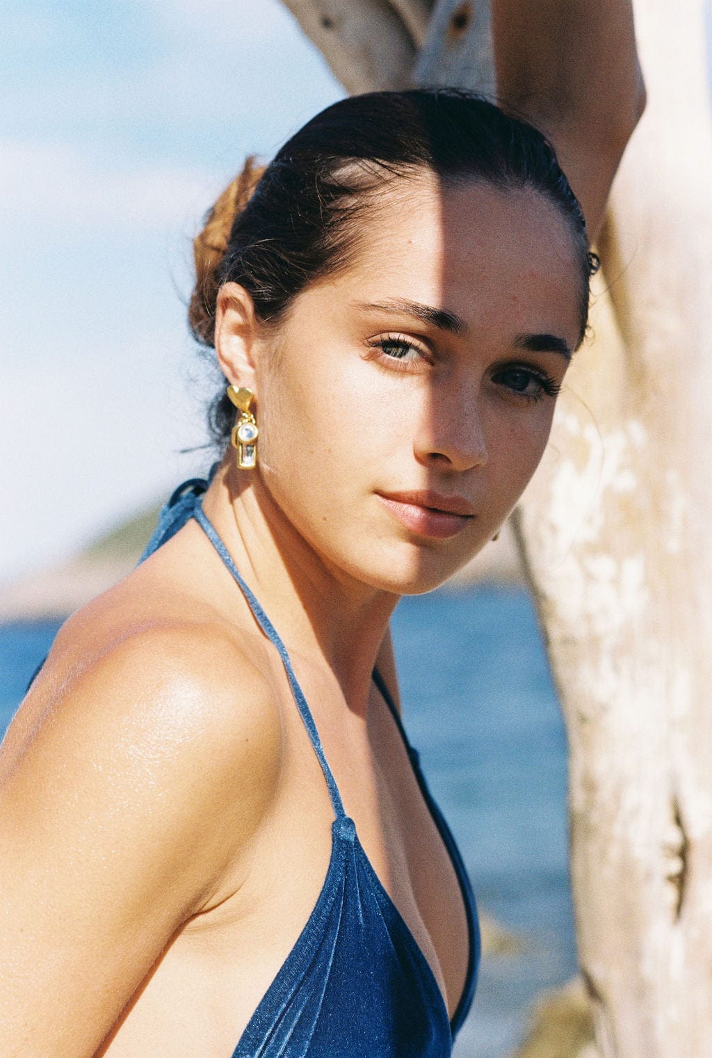 Gold-toned drop earrings with white pearl accent worn by woman at beach.