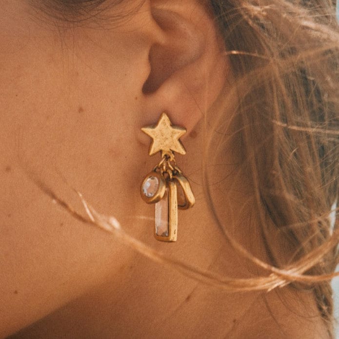 Gold star earring with dangling rectangular and oval charms worn on ear.