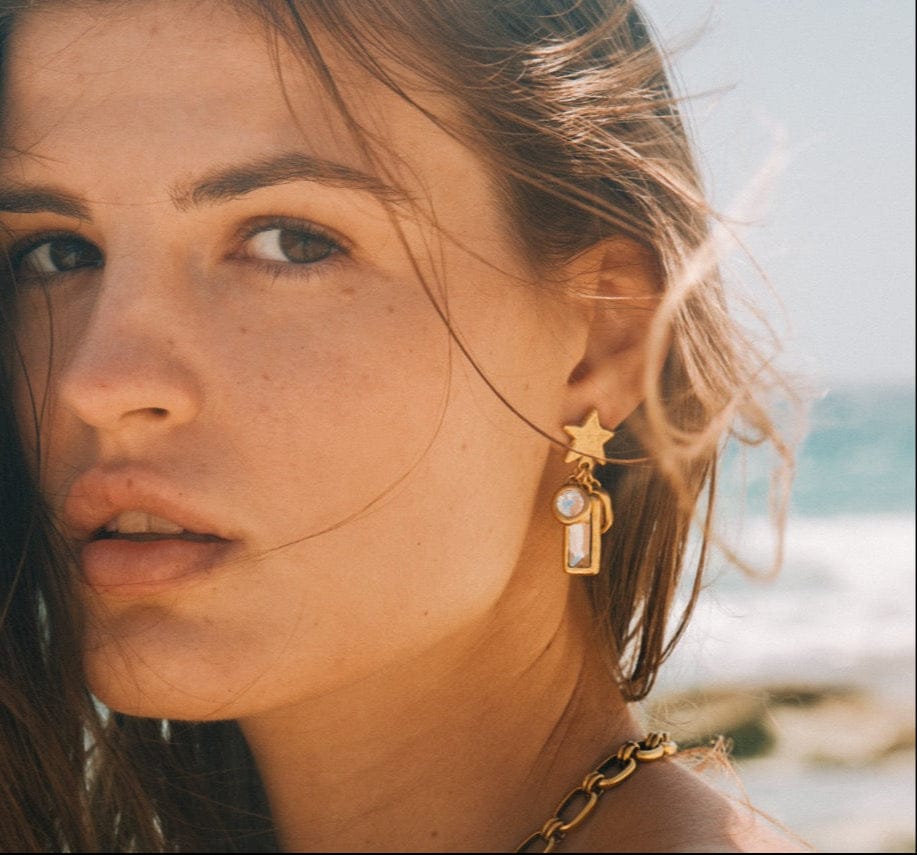 Gold star-shaped earrings with pearl and rectangular stone pendant drops worn on model.