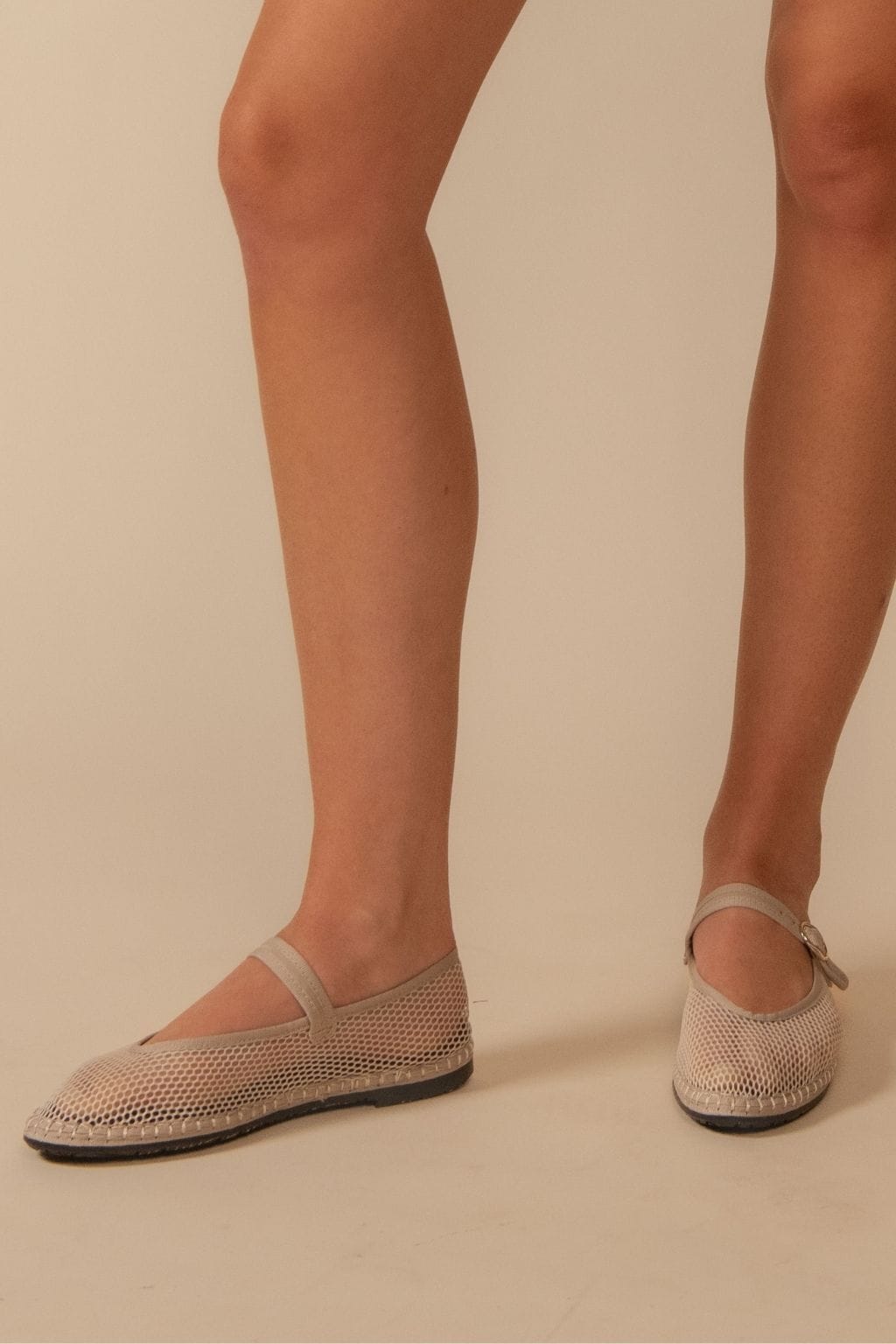 Nude mesh Mary Jane flats with ankle straps and dark soles, shown on model's feet.