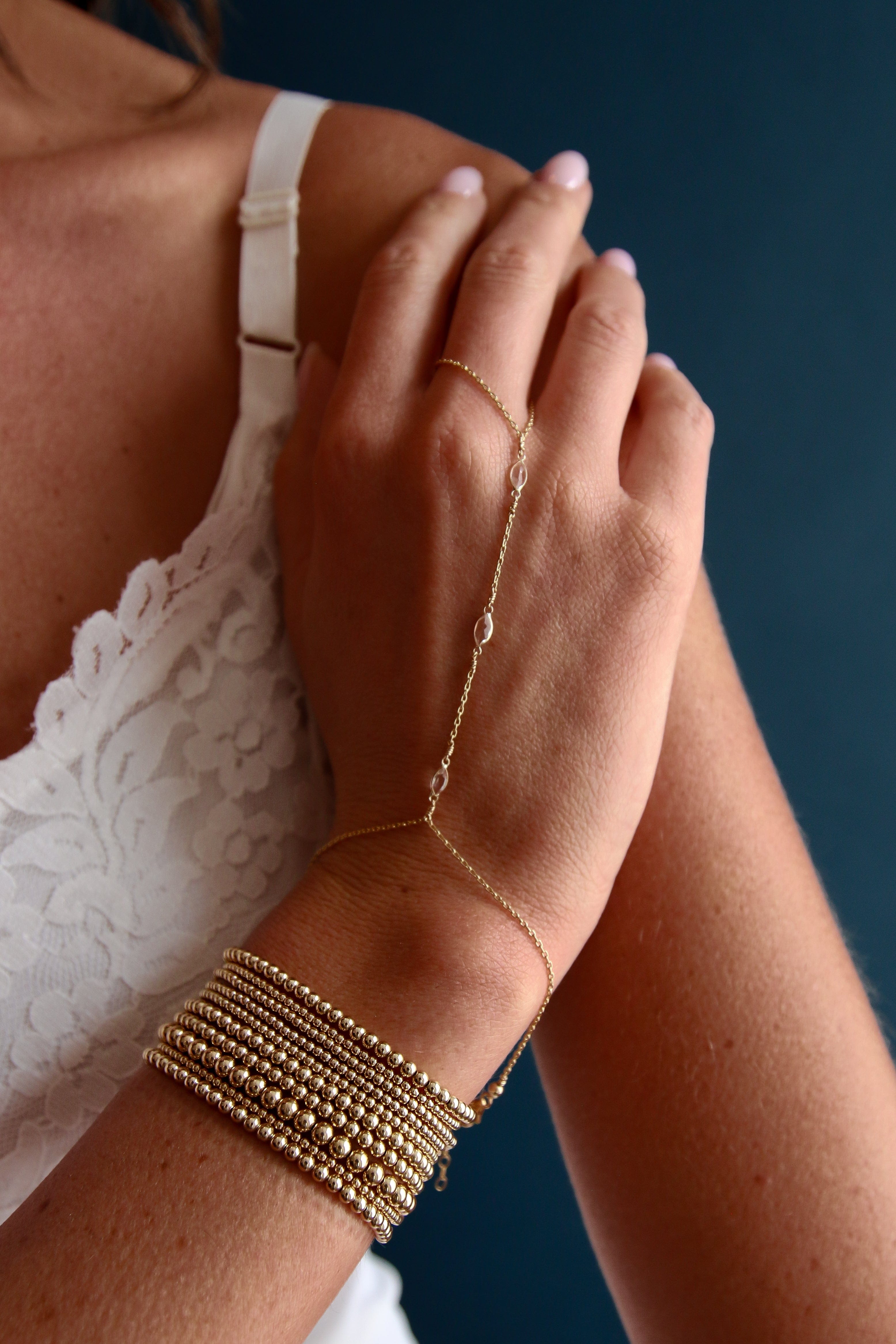 Gold-tone beaded bracelet with multiple thin strands worn on wrist with matching hand chain.