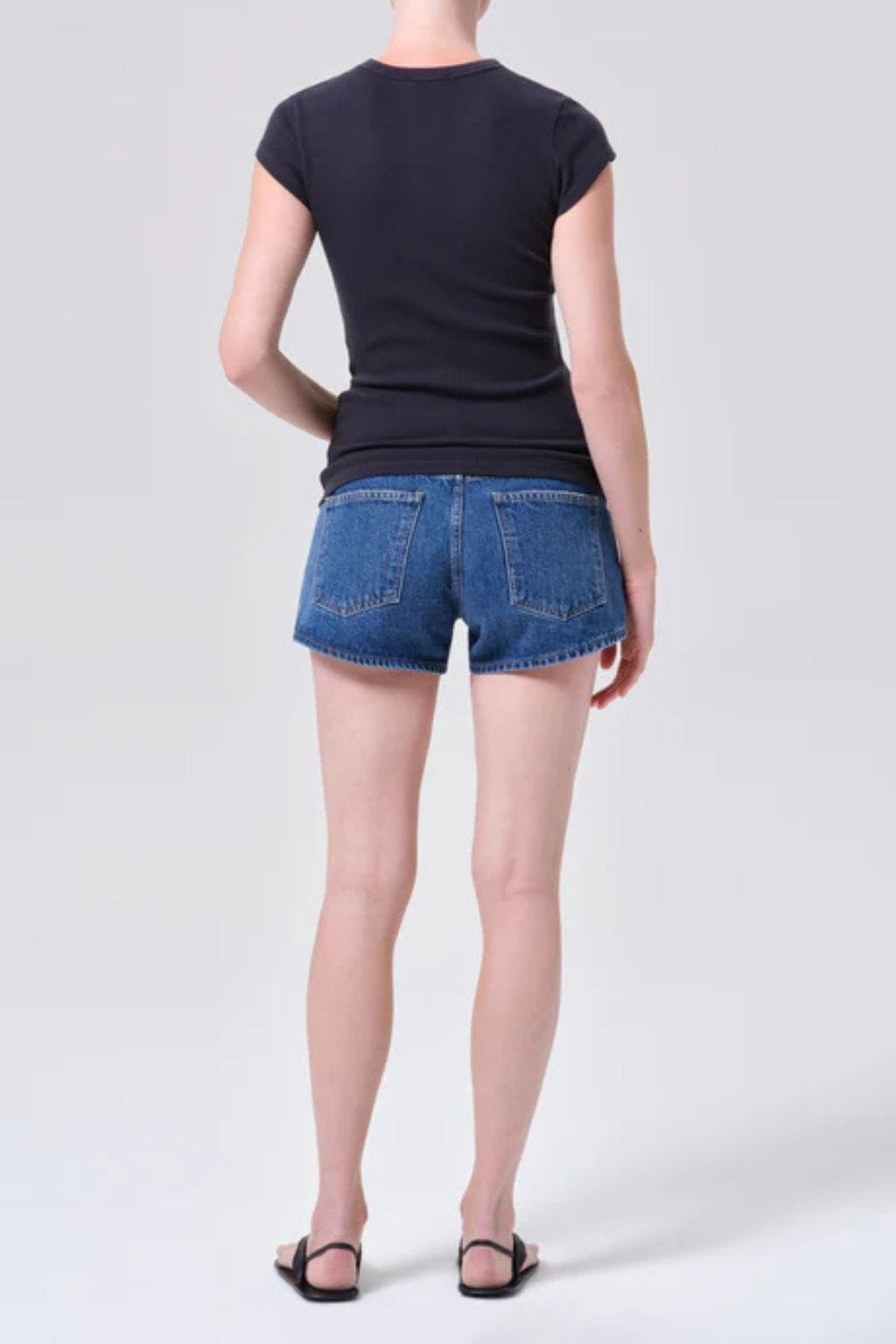 Woman wearing blue denim shorts with raw hem and black cap-sleeve top, shown from back.