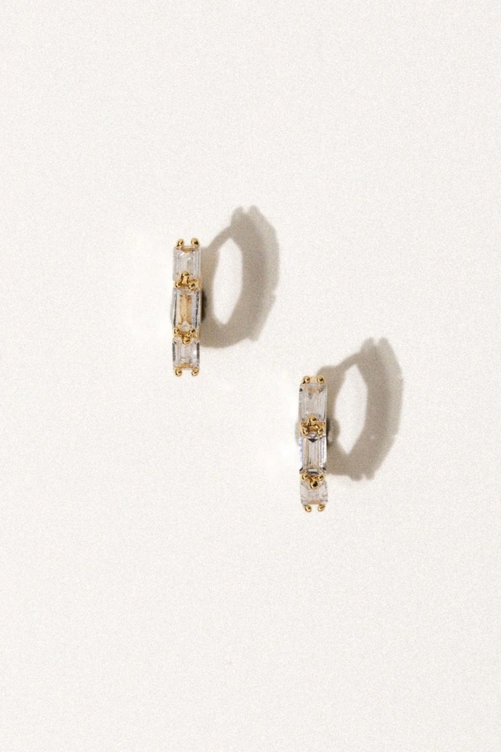 Gold huggies earrings with clear rectangular cubic zirconia stones set in metal settings, shown as a pair.
