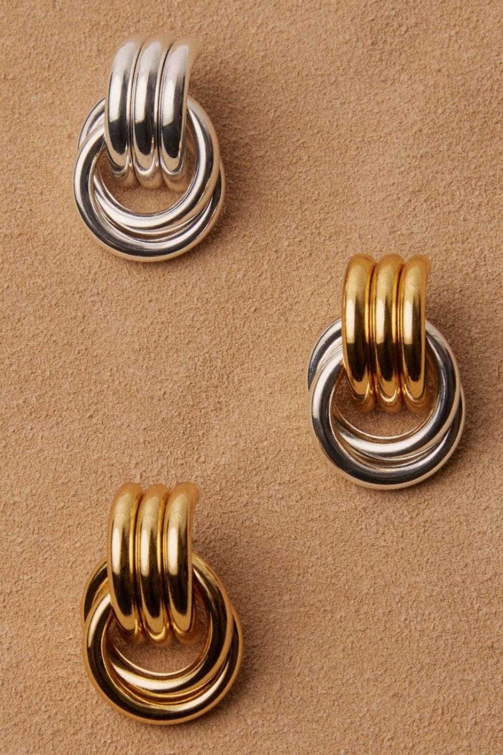 Three pairs of knot earrings in silver and gold tones with triple-loop designs on a neutral background.