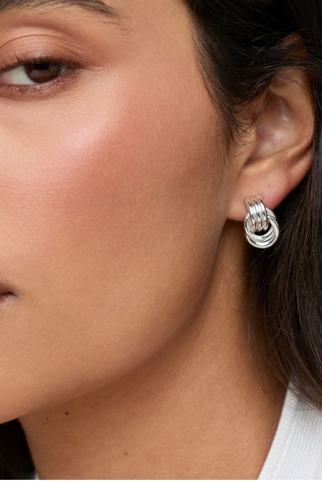 Silver knot stud earrings worn on a person's ear, featuring interlocking curved bands.