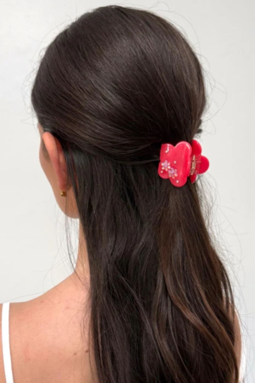 Red flower-shaped hair clip with beaded details worn in long dark hair.