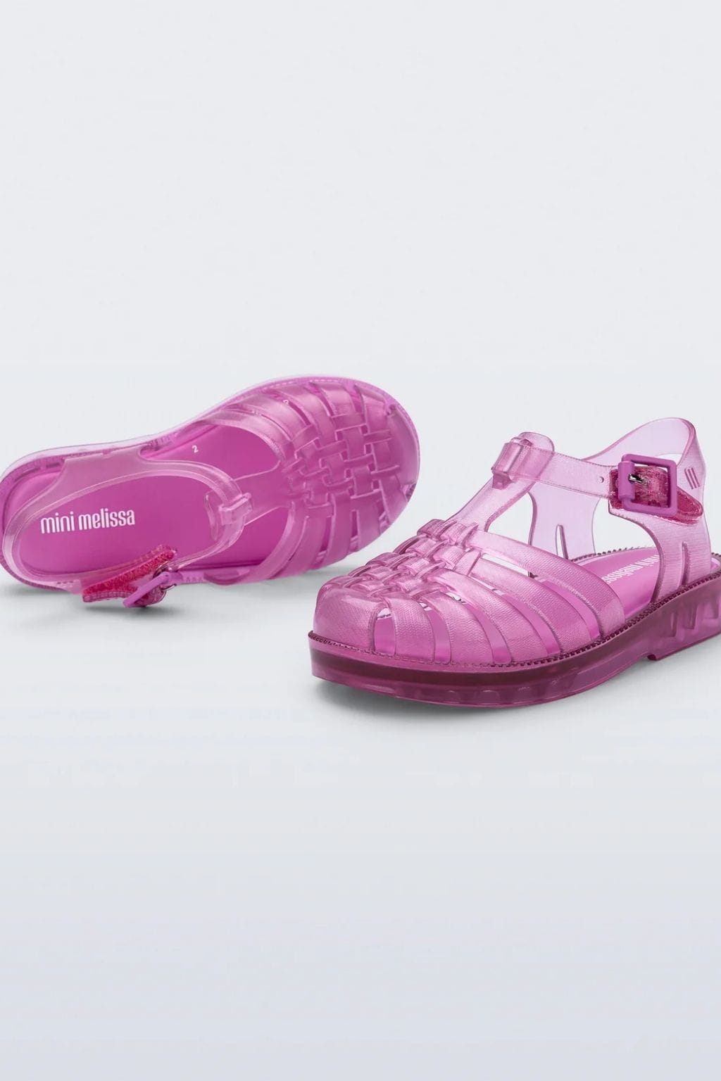 Transparent pink jelly sandal with closed toe, buckle strap, and textured sole, shown from top and side angles.