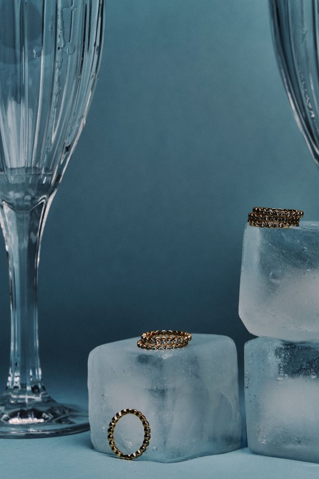 Gold-toned textured rings displayed on frosted acrylic blocks next to a crystal glass.