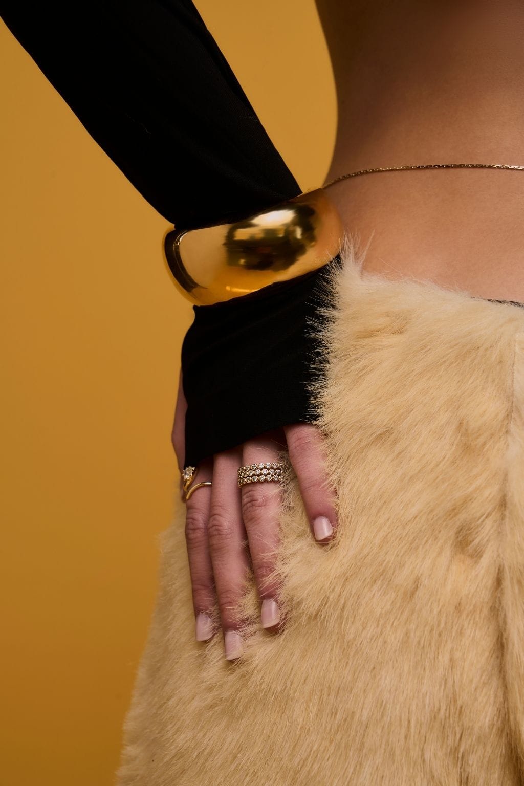 Gold-toned stacked ring worn on model's hand against yellow background.