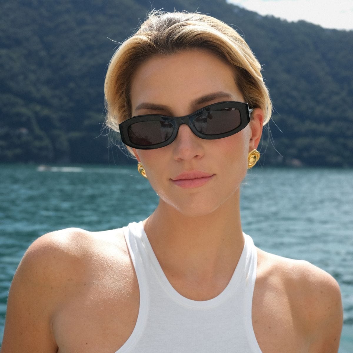 Black oval sunglasses with dark lenses worn by a woman outdoors.