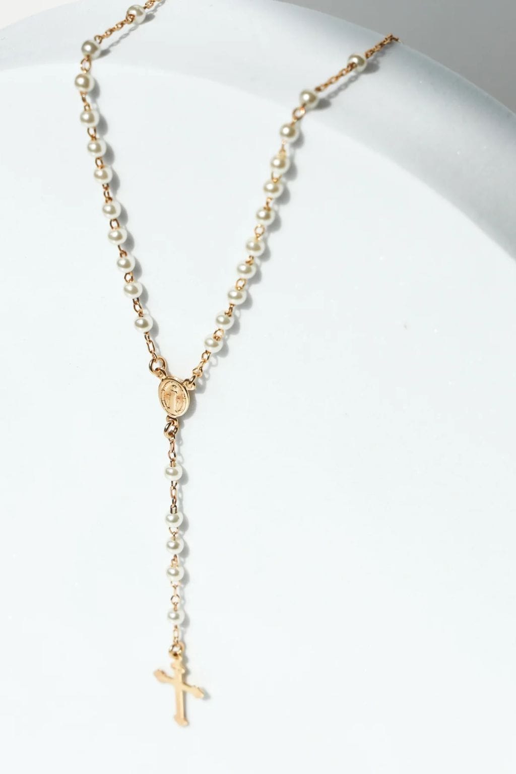 Gold-toned rosary necklace with cream pearls, oval medallion centerpiece, and cross pendant.