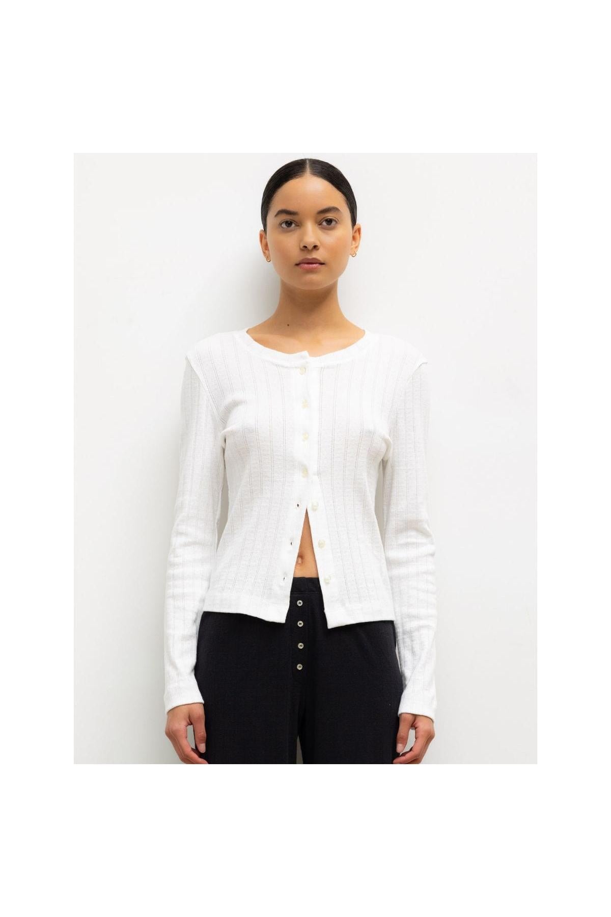 White pointelle crew cardigan with button front closure and long sleeves worn over black pants.