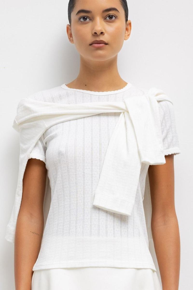 White pointelle short-sleeve tee with draped fabric detail across chest and fitted silhouette.