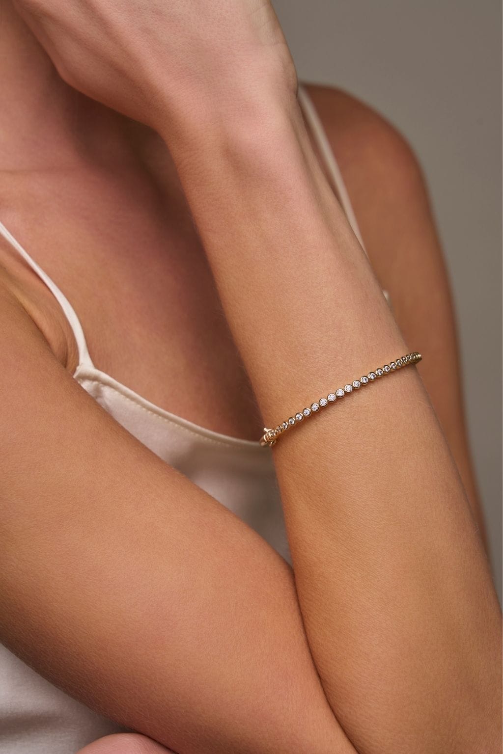 A slender gold bangle set with a row of small round clear stones rests on a woman's wrist.