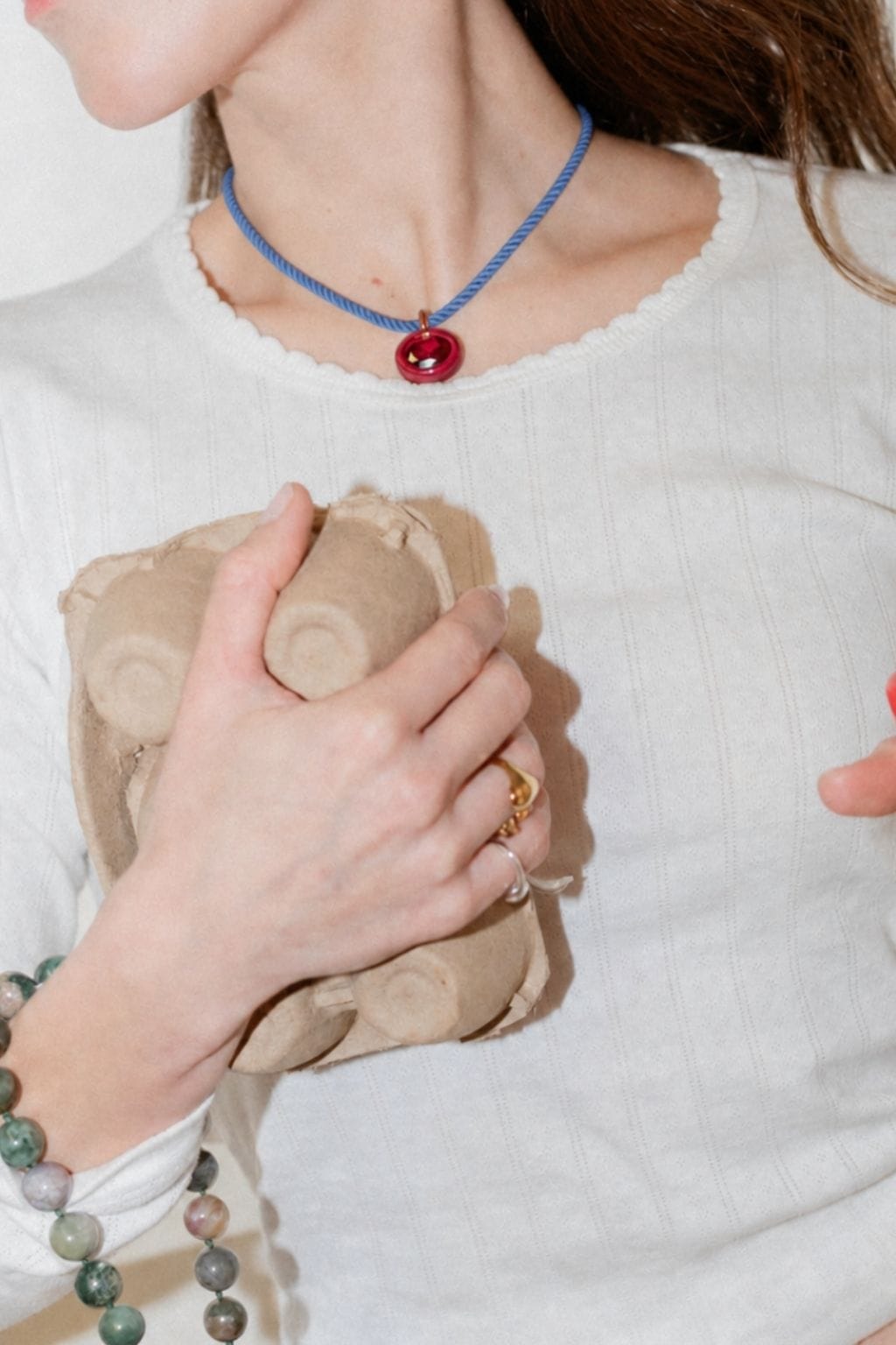 Blue rope necklace with red circular pendant worn close to the neck.