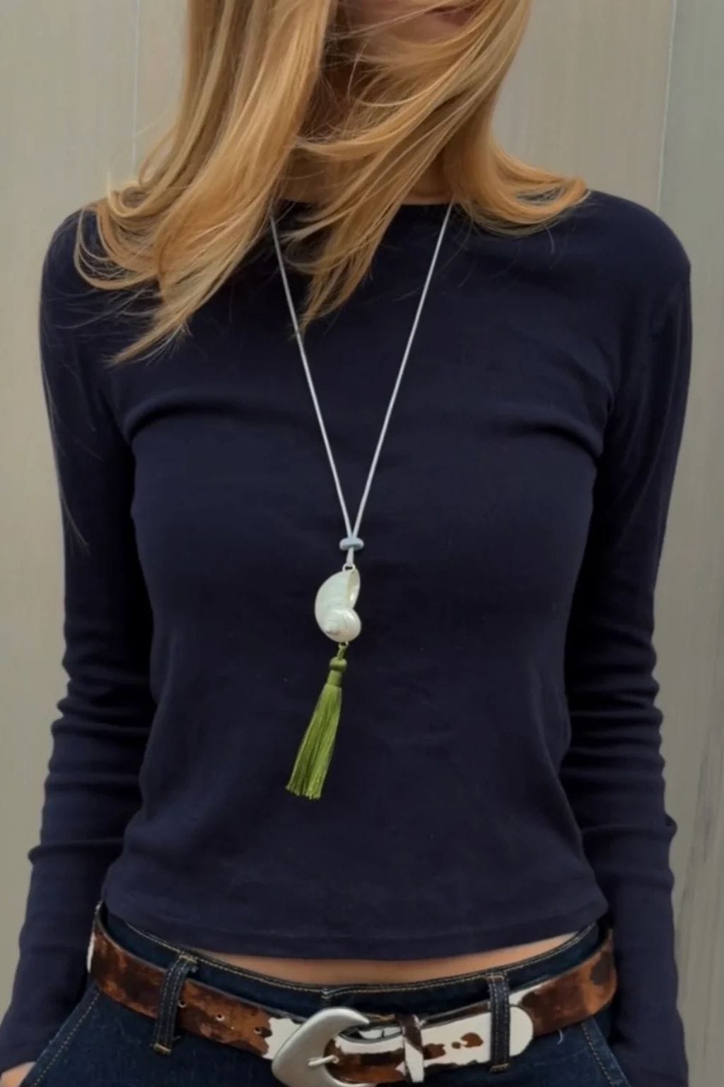 Long silver chain necklace with white curved pendant and green tassel hanging at center chest.