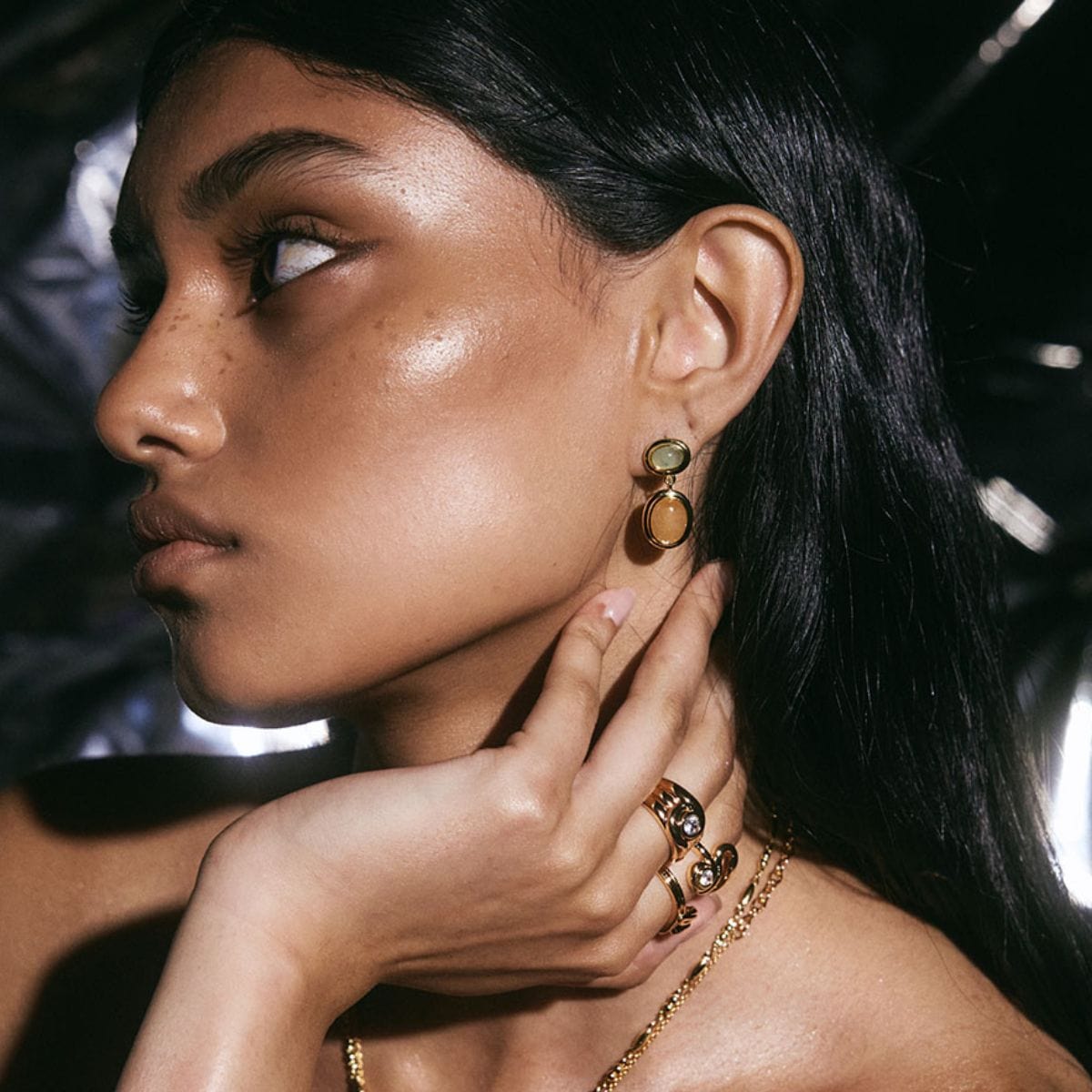 Gold-toned stud earrings with two stacked round stones in amber and warm brown tones worn on model's ear.
