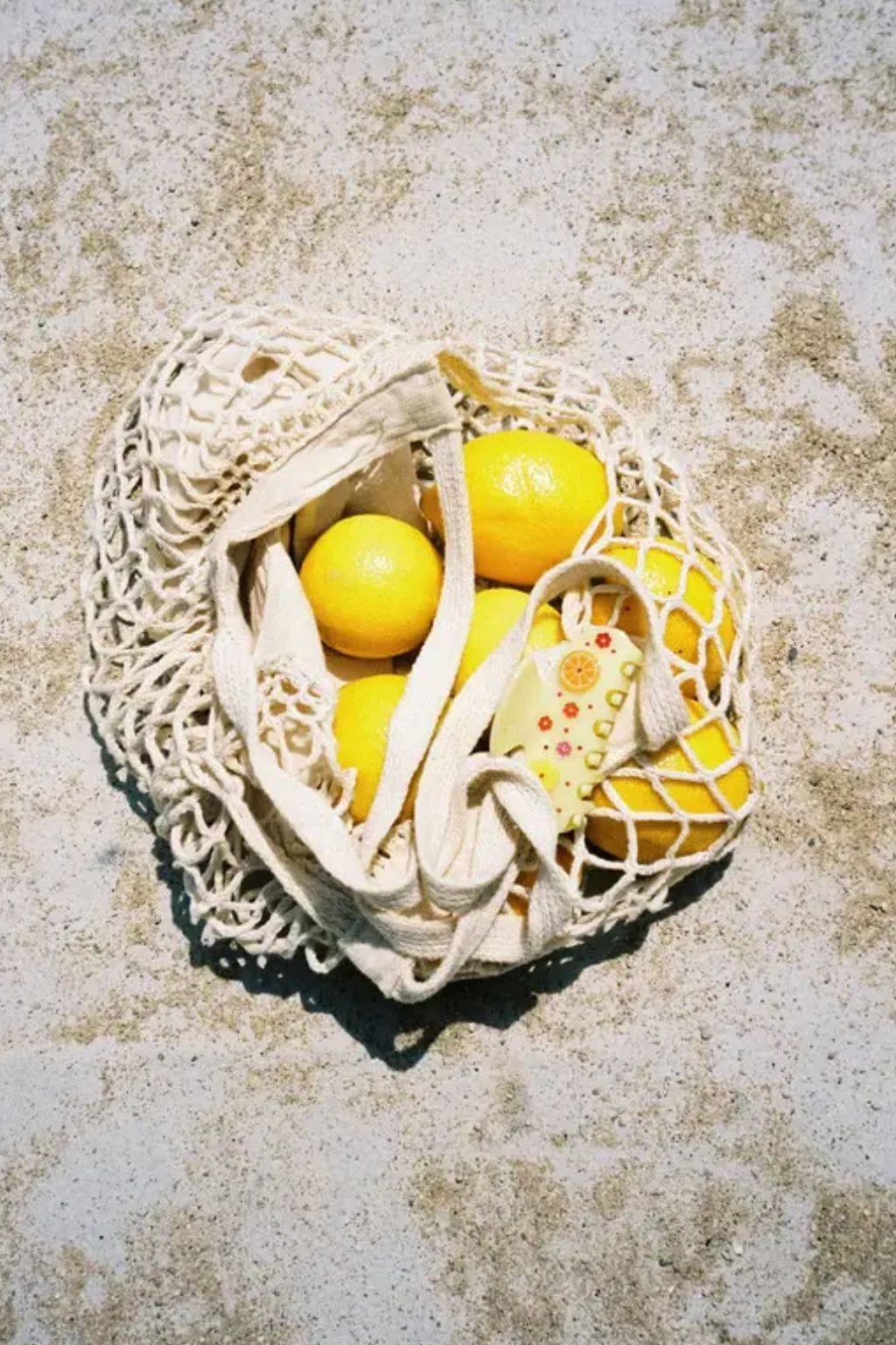 Cream-colored hair clip with sweetheart shape containing yellow lemons and decorative beads inside mesh pouch.