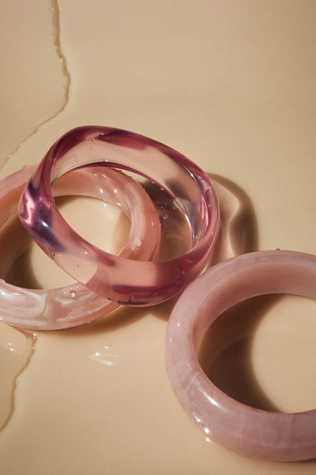 Three pink translucent resin bangles in varying shades stacked together on a neutral background.