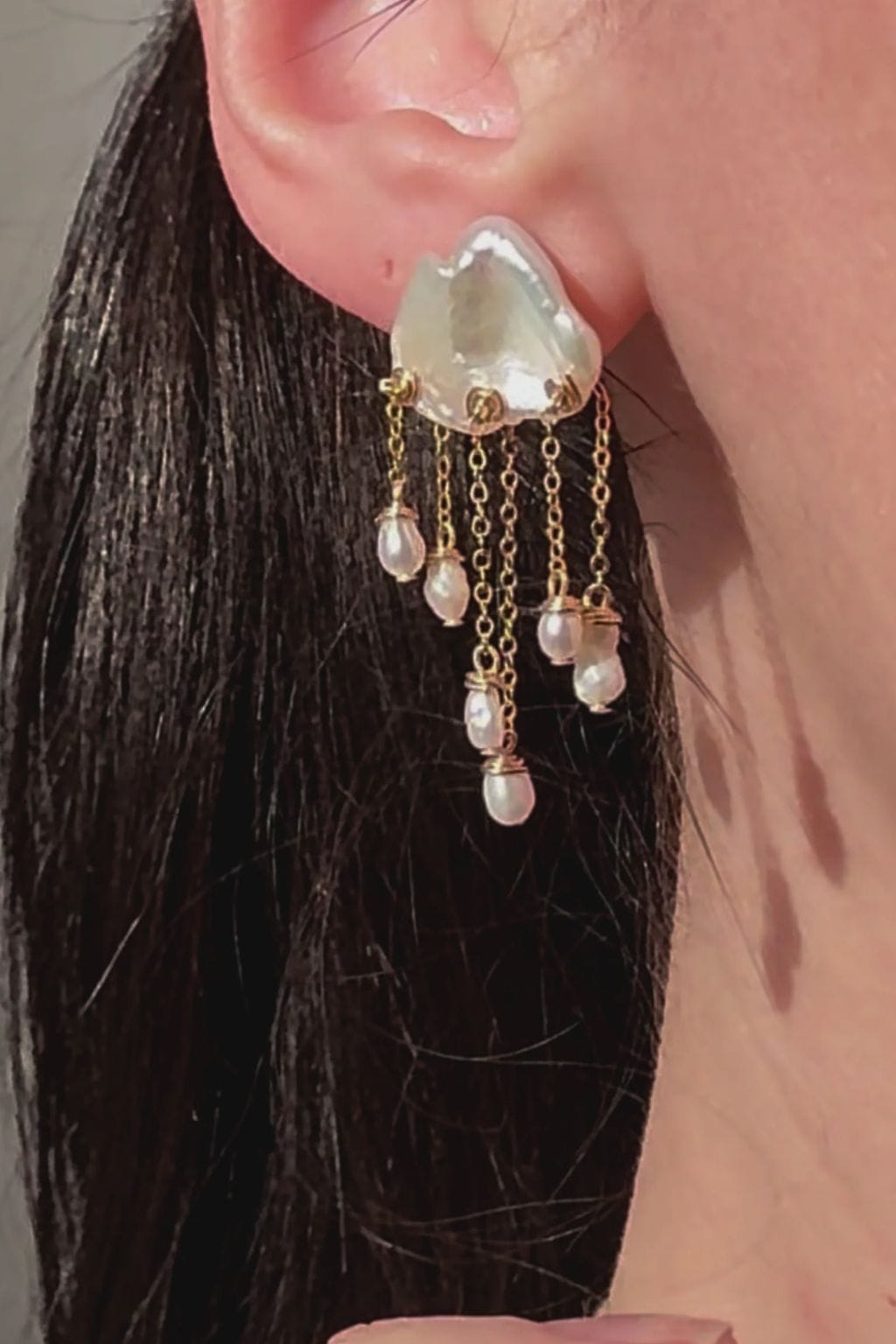 White teardrop earrings with dangling beads on gold chain accents, worn on ear.