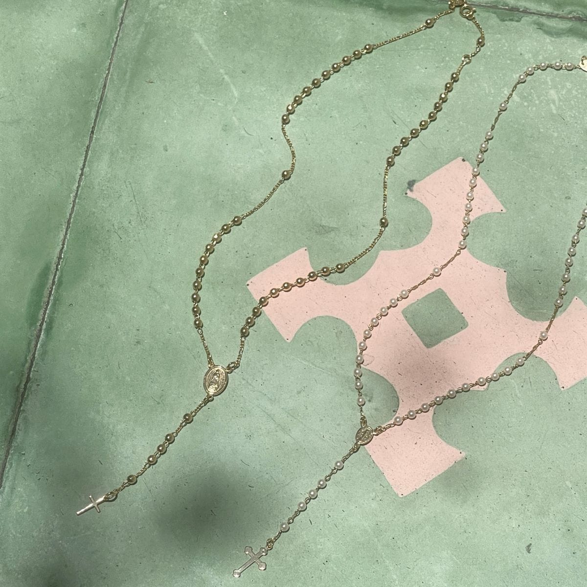Gold-toned rosary with pearl beads and cross pendant displayed on green surface.