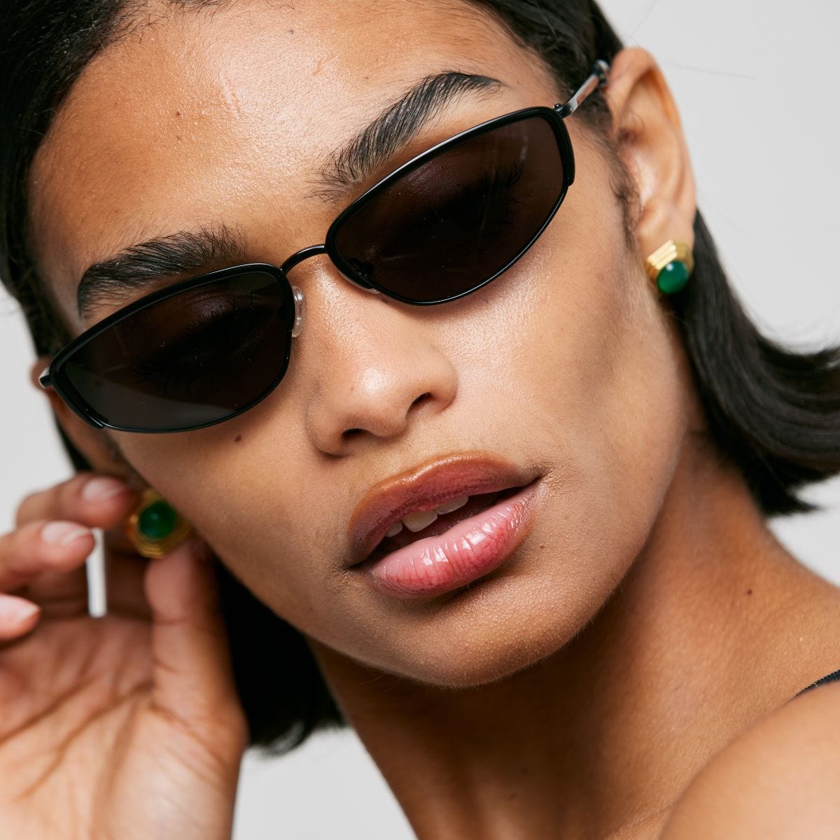 Black oval sunglasses with dark lenses worn by a person against a white background.