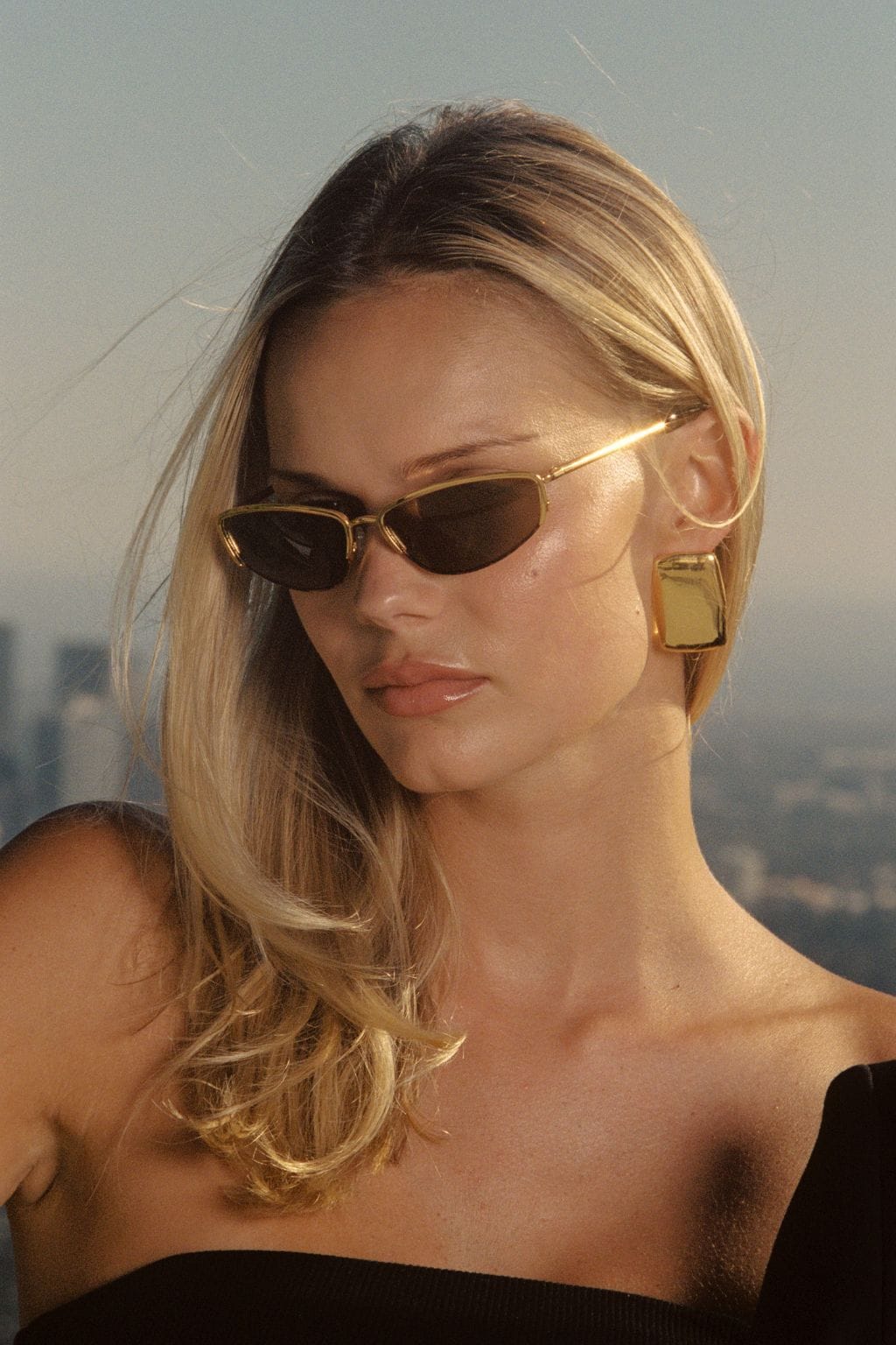 Tortoise and gold-tone oval sunglasses with dark lenses worn by a woman against a neutral background.