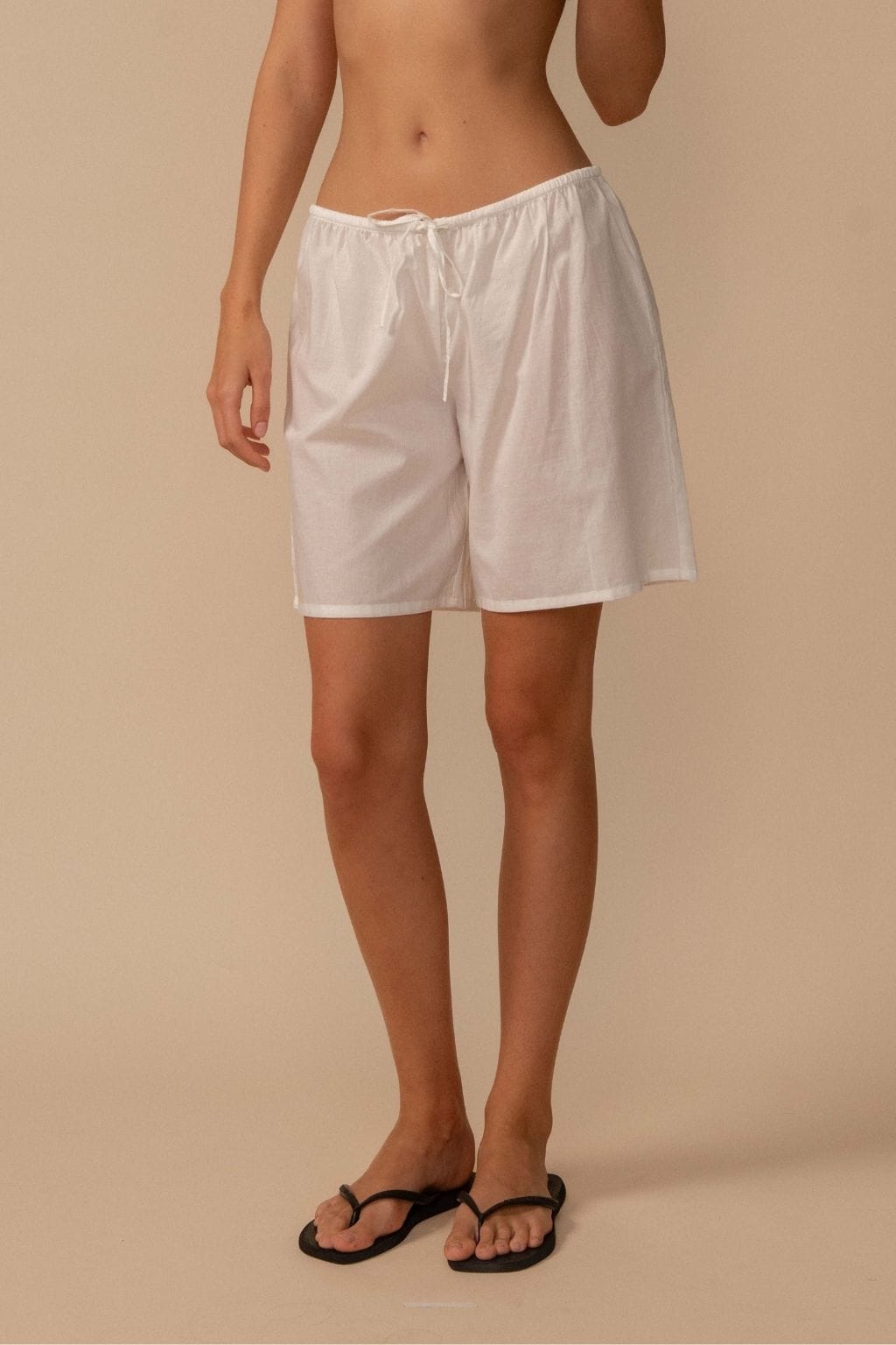 White cotton shorts with drawstring waist, knee-length, worn with black slide sandals.